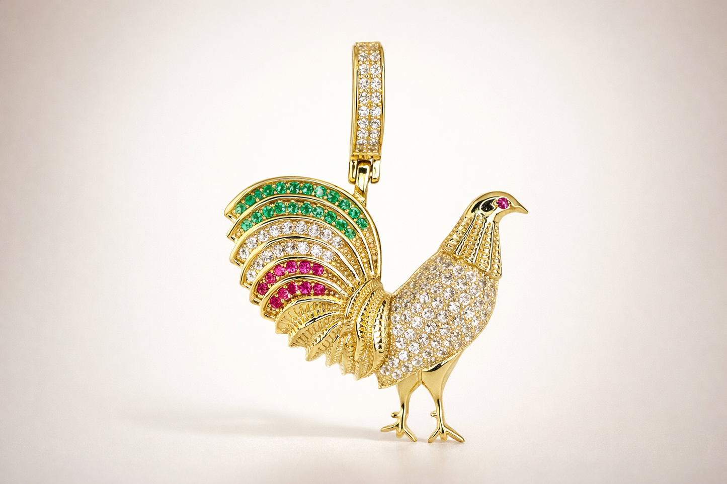 Gold rooster-shaped pendant with green white and red gemstone accents on a beige background